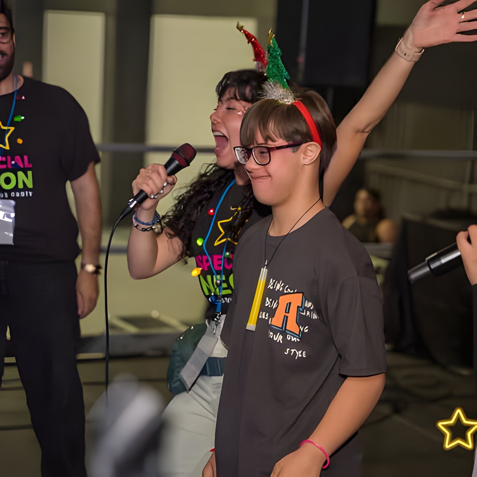 Un invitado canta en el escenario junto a una persona del equipo